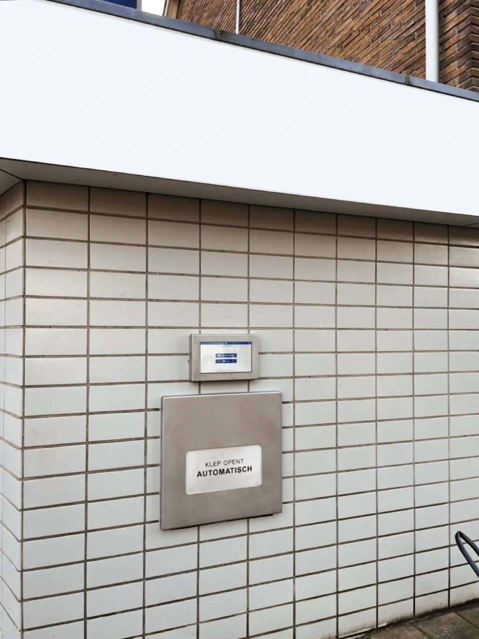 Automatische afhaalklep aan een betegelde muur, met een scherm erboven voor bediening en instructies.
