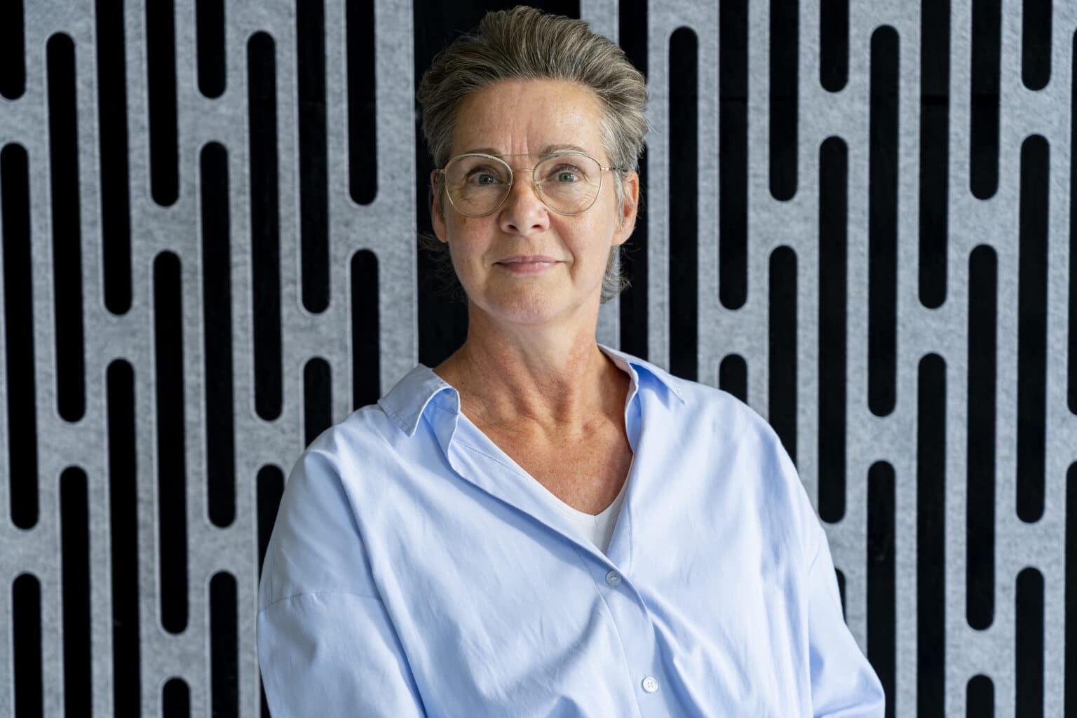 Ingrid, operationeel manager bij Pharmatool, poseert met een rustige en zelfverzekerde uitstraling voor een modern zwart-grijs patroon op de achtergrond.