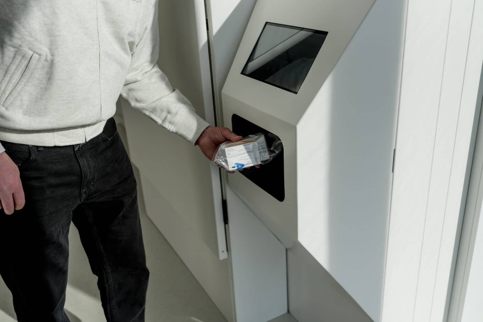 Persoon haalt verpakte medicatie op uit een 24/7 medicijnuitgifteautomaat met touchscreen in de apotheek.